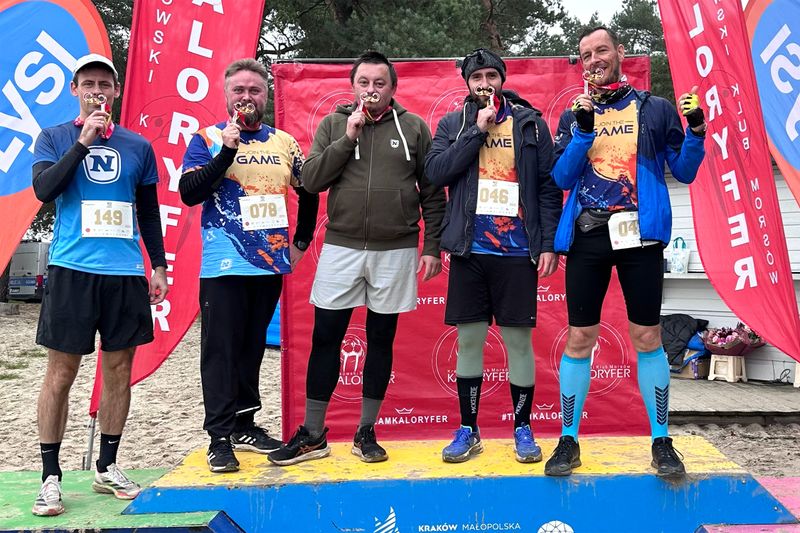 Pracownicy Novomatic Technologies Poland pozują na podium z rekwizytami w kształcie wąsów.