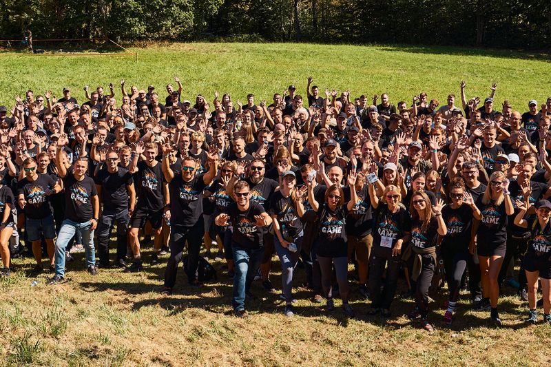 Widok z lotu ptaka na pracowników NTP wiwatujących z podniesionymi rękami podczas plenerowego eventu integracyjnego.
