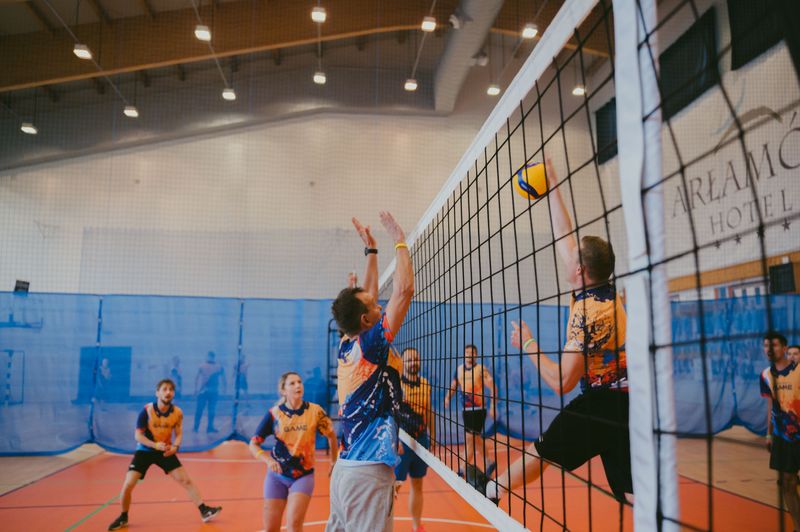 Pracownicy Novomatic Technologies Poland wyskakujący nad siatkę podczas zaciętego meczu siatkówki.