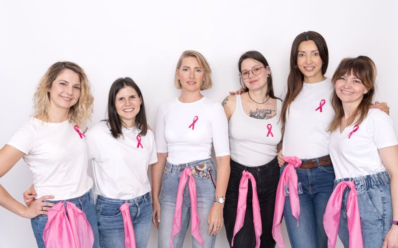 Pracowniczki NTP w białych koszulkach i z różowymi wstążkami, promujące profilaktykę raka piersi.