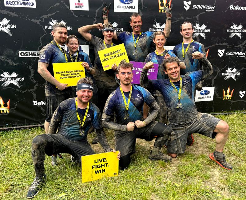 Nasi pracownicy umazani błotem i prężący muskuły po zakończeniu biegu Runmageddon.