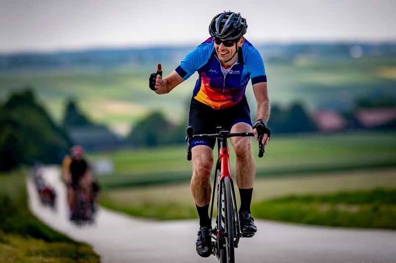 Rowerzysta z Novomatic Technologies Poland zmagający się z pagórkowatym terenem i pokazujący kciuk w górę do kamery.